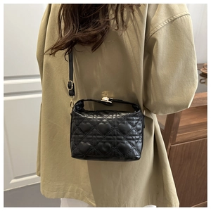 Rear view of a black heart-quilted leather handbag with gold clasp worn by a model