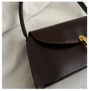 Detailed close-up of dark brown leather texture and golden metal twist lock on baguette bag