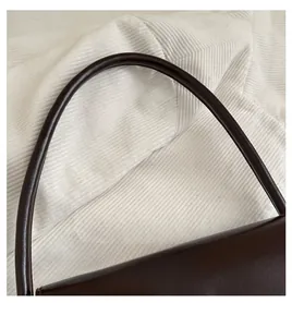 Detail view of the smooth dark brown leather handle and thick texture of the handbag