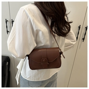 Close-up of brown faux leather crossbody bag with decorative buckle and flap closure