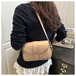 Detail of a chic cream crossbody bag with leather texture worn by a model in a room