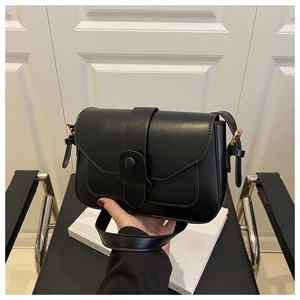 Detail of minimalist black matte crossbody bag with gold snap closure and leather strap
