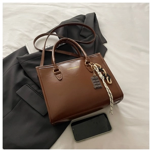 Détail du sac en cuir marron avec lettrage doré, poignées et breloque en chocolat