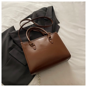 Detail of a brown leather tote bag with gold metal buckles and adjustable shoulder strap