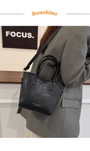 Detail of black pebbled leather tote bag with gold lettering and slim shoulder strap