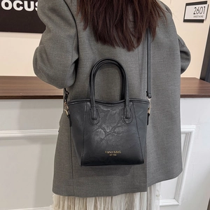Minimalist black leather tote bag with gold lettering and adjustable shoulder strap