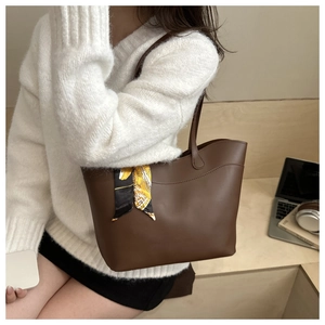 Brown leather tote bag with decorative silk scarf shown in a stylish office setting