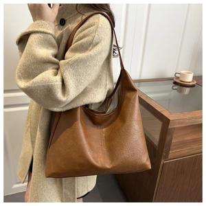 Detail view of large caramel brown leather tote bag texture on a beige wool coat