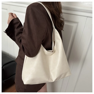 Side view of an oversized cream faux leather tote bag worn with a brown blazer