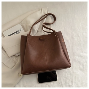 Detail view of large brown tote bag showing pebbled leather texture and metal rivet buckle