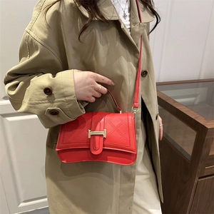 Fashionable red quilted crossbody bag with gold H-buckle shown on a stylish trench coat outfit