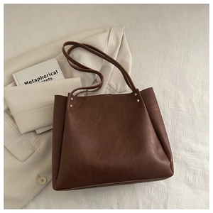 Detail of vintage brown leather tote bag showing golden rivets and wide shoulder straps