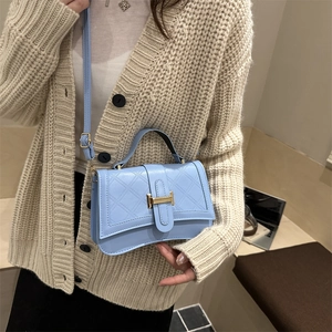 Quilted light blue leather crossbody bag with gold H-buckle worn by woman in knitwear