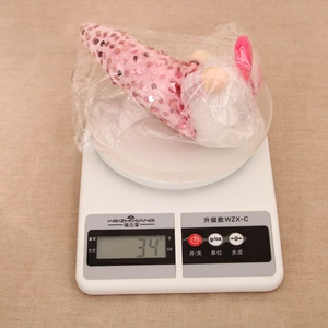 Detail shot of a plush sequined doll being weighed, showing 34g on a digital scale