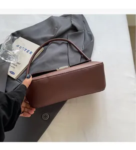 Brown faux leather baguette bag with magnetic closure held against a grey suit jacket