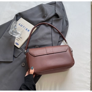Detail of deep brown matte PU leather shoulder bag on a dark grey blazer backdrop