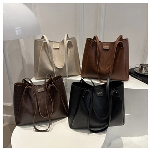 Four minimalist tote bags in beige, brown, and black displayed on modern stands