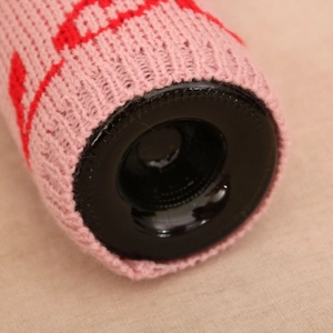 Détail du cache-bouteille tricoté rose avec motif de cœur rouge sur une bouteille sombre