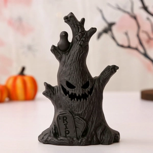 Detail of spooky black dead tree sculpture with hollow ghost face and RIP tombstone