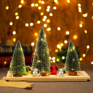 Primer plano de mini árboles de Navidad iluminados con nieve sobre bandeja de madera
