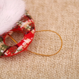 Close-up of red and green plaid fabric ornament with white faux fur trim and gold string