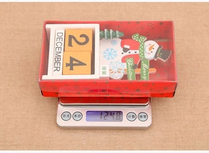 Wooden snowman calendar on a digital scale showing weight in branded packaging