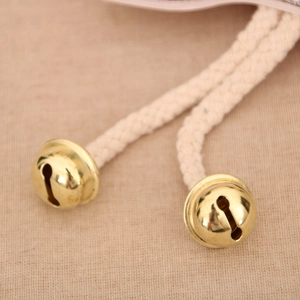 Macro detail of polished gold metal bells with off-white braided rope Christmas ornaments