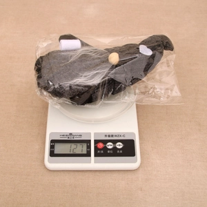 Détail d'un gnome de Noël gris tricoté montrant un poids de 127g sur une balance précise