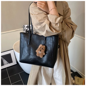 Detail of a black leather tote bag featuring white text and a brown teddy bear charm