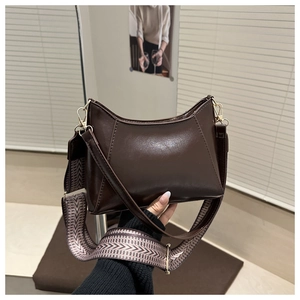 Détail d'un sac en cuir marron foncé avec bandoulière tissée colorée et boucles dorées chic