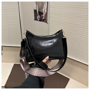 Détail d'un sac à main en cuir verni noir avec boucles dorées et bandoulière tissée