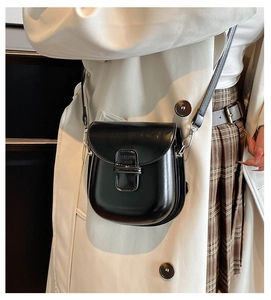 Detail of glossy black leather crossbody bag with silver hardware on a model