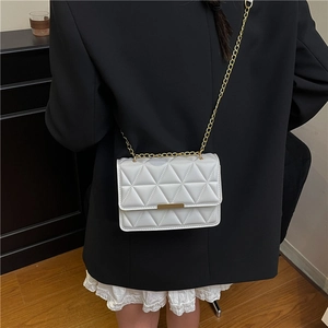 Elegante borsa trapuntata bianca con catena dorata su un blazer nero dallo stile minimal