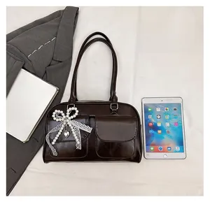 Détail d'un sac à main marron foncé avec nœud en perles et pendentif cœur sur costume