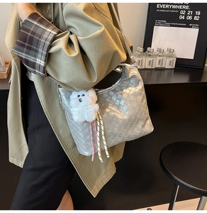 Silver woven leather hobo bag with plush bear charm styled with a khaki trench coat