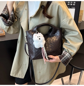 Close-up of dark brown woven bucket bag featuring a cute white plush puppy charm and leather strap