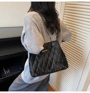 Detail of large black quilted tote bag with golden metal chain strap on model