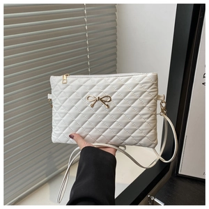 Close-up of white quilted square crossbody bag featuring a golden bow metal buckle