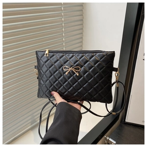 Detailed view of black quilted crossbody bag with gold bow clasp and metal zipper