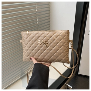 Detail of light brown quilted crossbody bag with gold bow clasp and shoulder strap