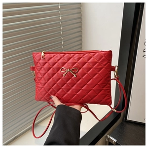 Close-up of red quilted crossbody bag featuring a golden bow metal accessory and zipper