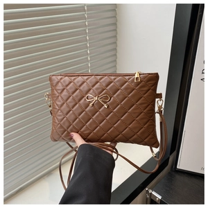 Detail of brown quilted faux leather crossbody bag with a gold bow metal ornament