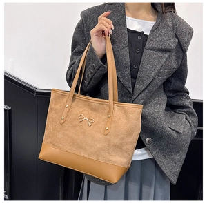 Sac cabas en daim marron avec empiècement cuir et nœud doré porté par un mannequin