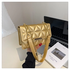 Close-up of golden quilted crossbody bag with triangle stitching and metal chain strap