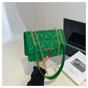 Detail of green quilted chain bag with gold metal clasp on an office desk setting
