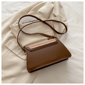 Detail of a brown leather bag featuring colorful woven edges on the flap and gold buckle