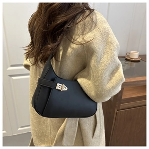 Side view of black crescent underarm bag with gold lock on a model in a warm cafe setting