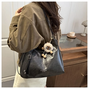Back view of a black leather tote bag with a cute bear pendant on a female model