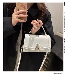Détail d'un sac à bandoulière blanc avec une boucle métallique dorée en forme de V