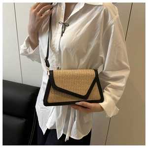 Detail of a handmade straw crossbody bag with black faux leather trim on a model